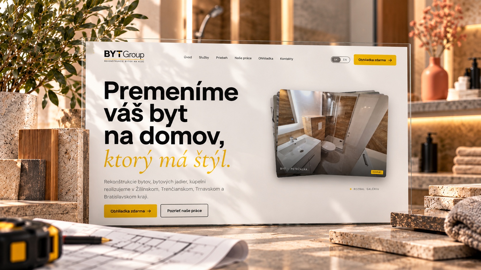 BYTGroup — úvodná stránka webu rekonštrukcií na obrazovke medzi vzorkami kameňa a dreva, metrom a stavebným výkresom